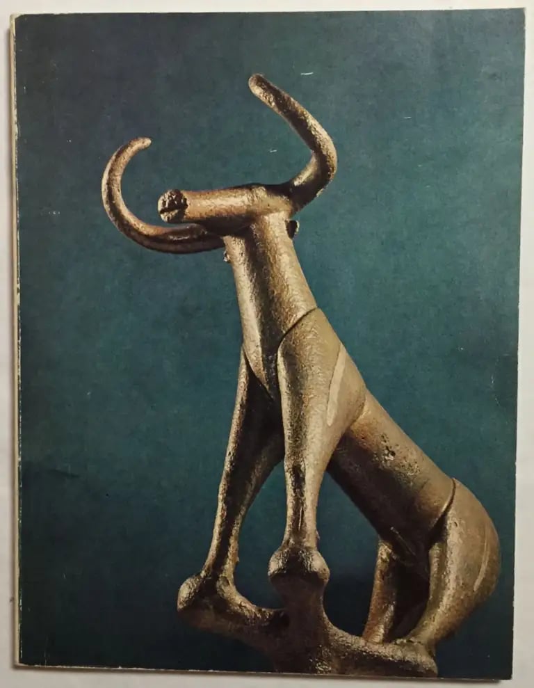 Ancient bronze bull sculpture featuring long horns and a slender body against a teal background.