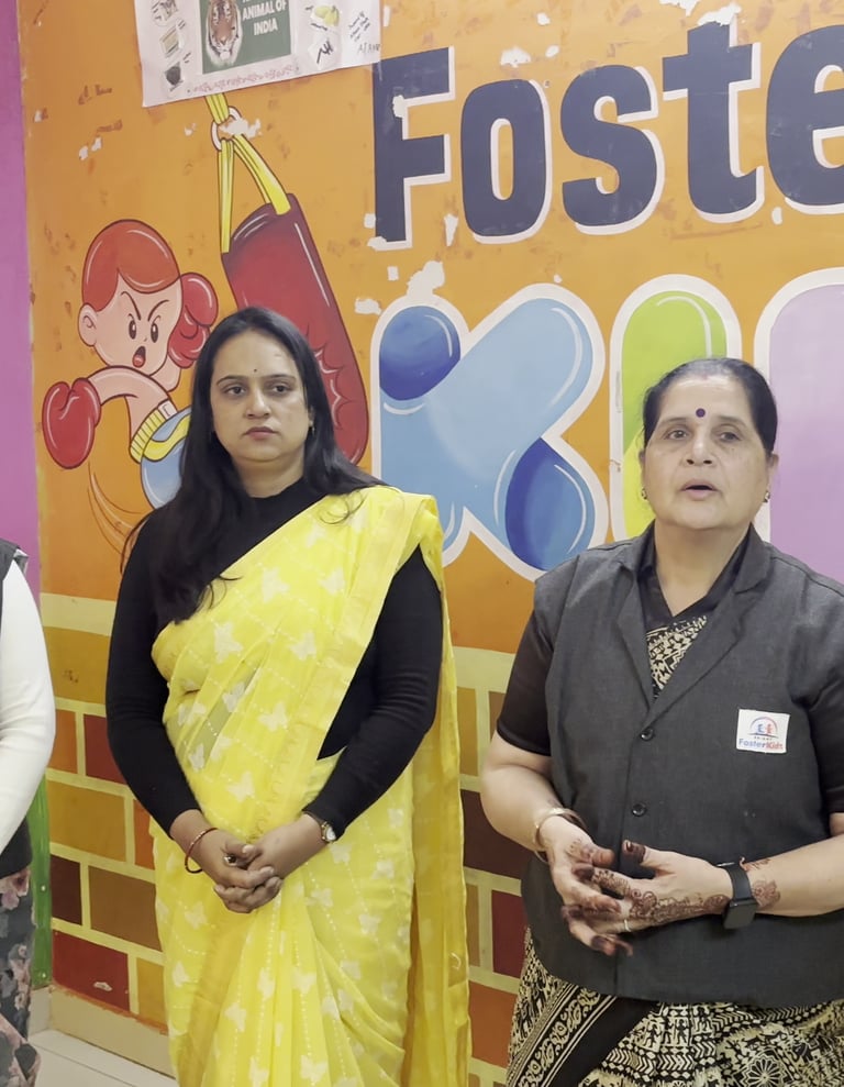 Preschool teachers at Foster Kids play school standing in a classroom with educational wall charts.