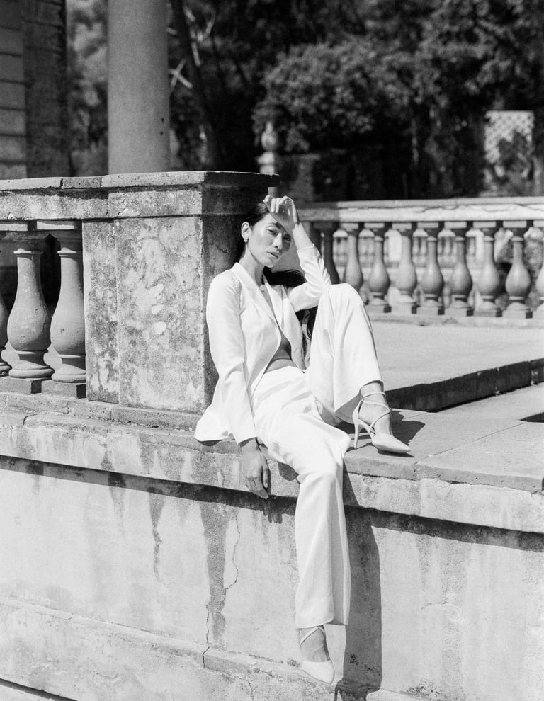 A classic woman sitting on a ledge in a minimalist suit.