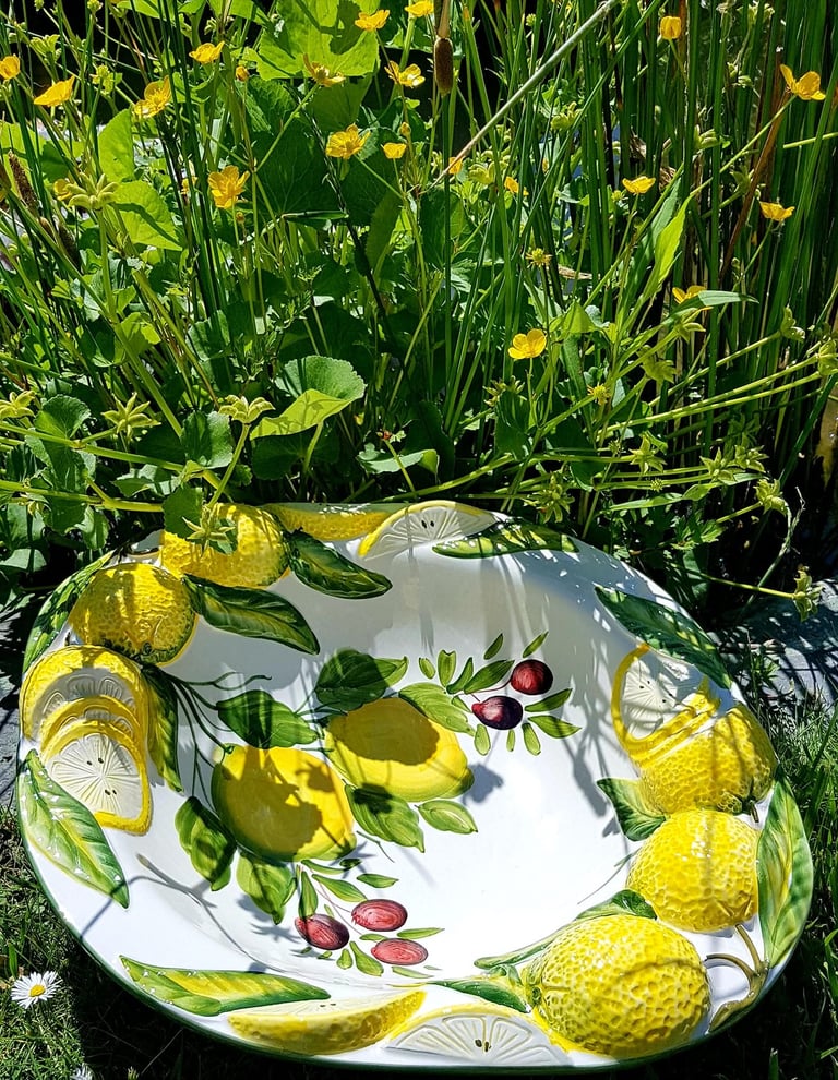 Hand-painted ceramic lemon bowl with olive branch relief in a garden of yellow wildflowers.