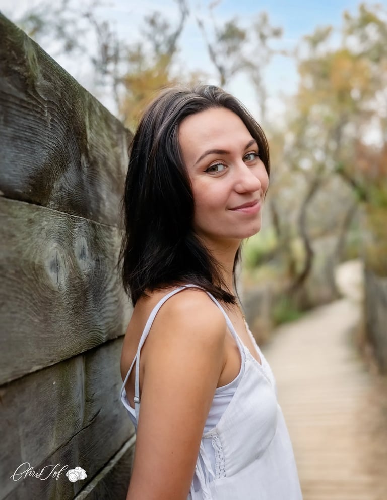 Portrait d'une femme brune souriante adossée à une palissade en bois sur un sentier à Canet 66