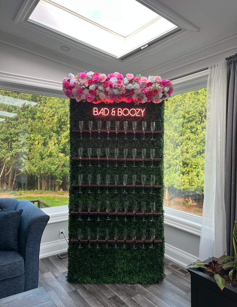 Champagne wall of assorted pink roses and a sign that says bad & Boozy
