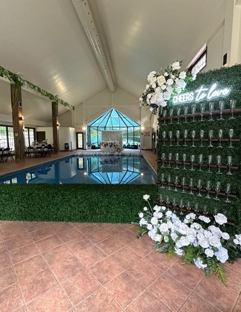 Wedding champagne wall set up with a cheers to love neon with white roses and greenery