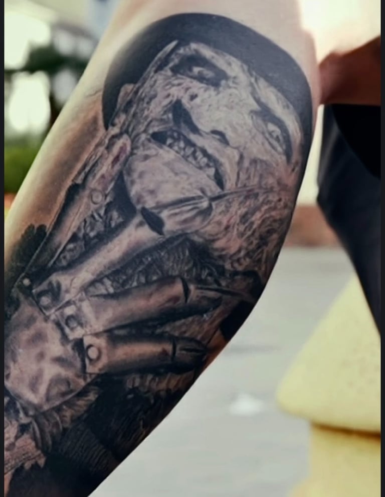 Realistic black and grey Freddy Krueger tattoo on an arm featuring his iconic bladed glove and burnt face.