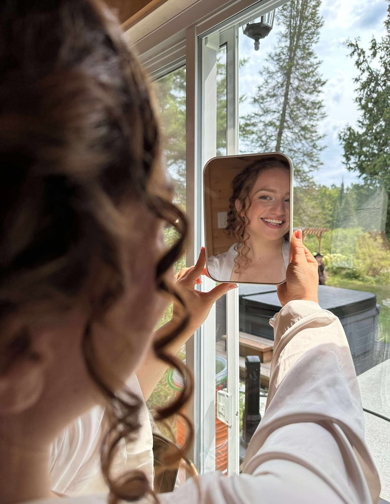 une mariée se regarde dans le miroir après son maquillage et sa coiffure et elle est heureuse