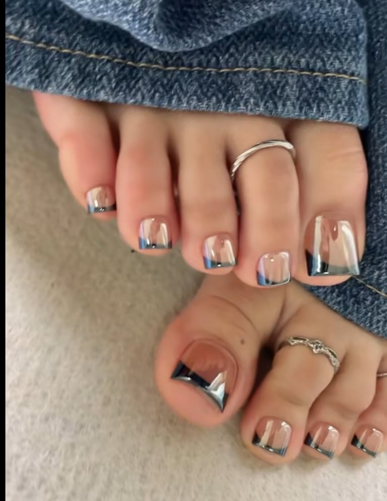 Pedicured toes featuring a chrome French tip design and silver toe rings with denim jeans.
