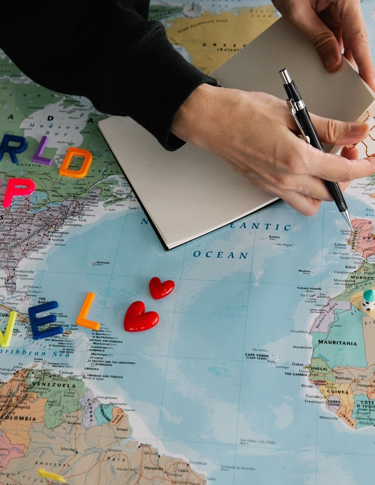 A person planning a trip on a world map with a notebook, pen, and colorful travel magnets.