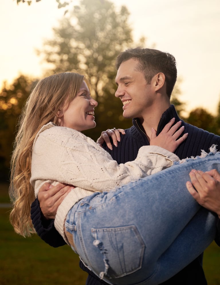 a man carring a woman in his arms in front of a tree and sunset