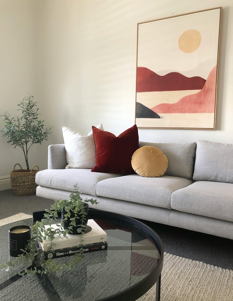 Glass coffee table styled with plant, decorative tray, and books in cozy living room.o