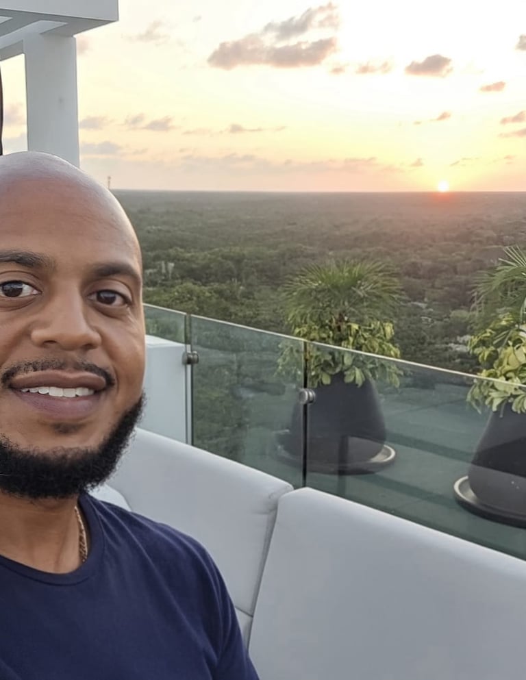 Smiling man taking a selfie on a luxury rooftop lounge at sunset overlooking a tropical forest.