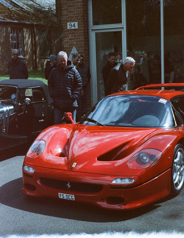 a red Ferrari F50 parked in front of a building, with a film burn at the bottom of the image