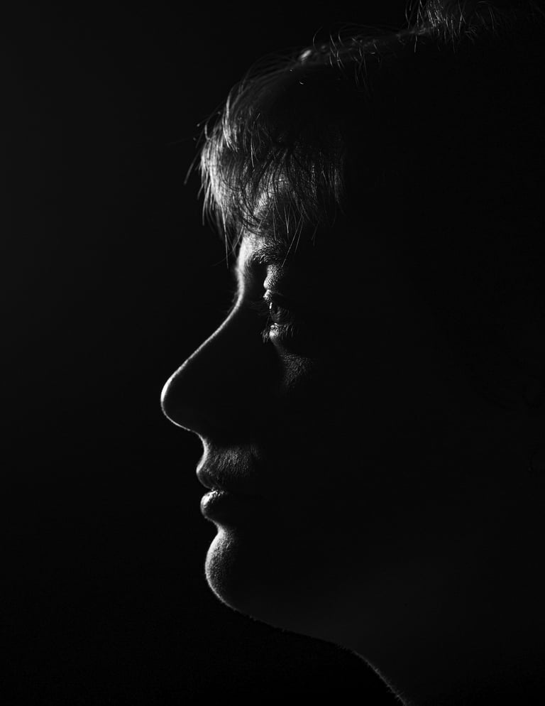 Dramatic black and white profile silhouette of a person's face against a dark background.