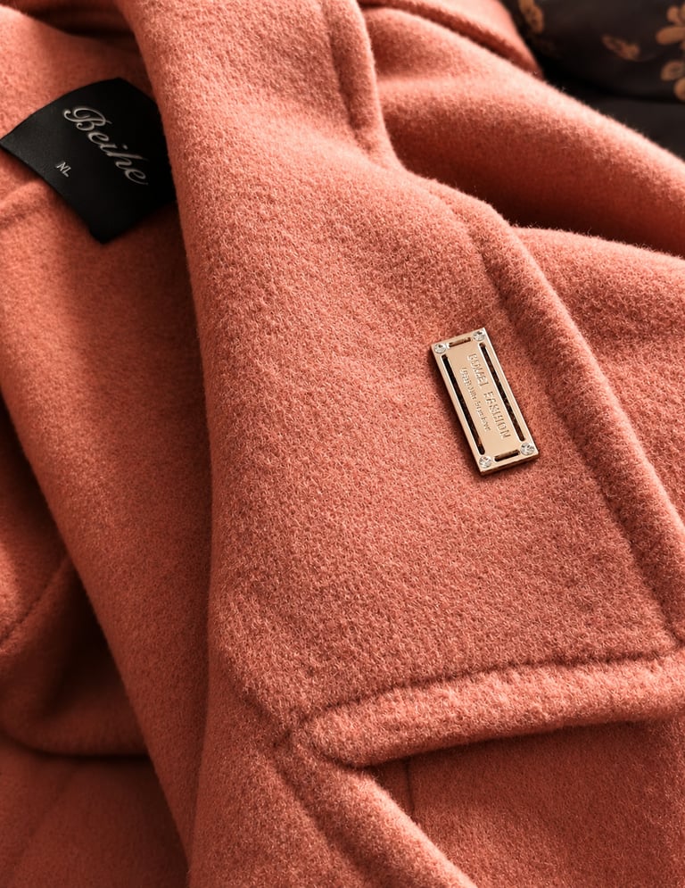 Rectangular metal logo plate attached to a coral wool coat