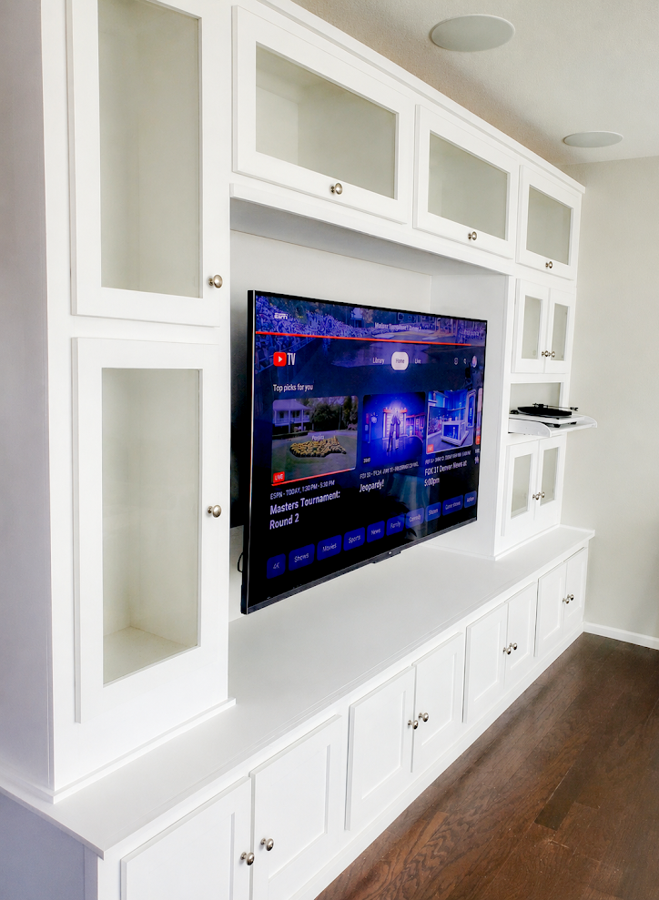 Modern white custom built-in entertainment center with glass cabinets and a wall-mounted TV.