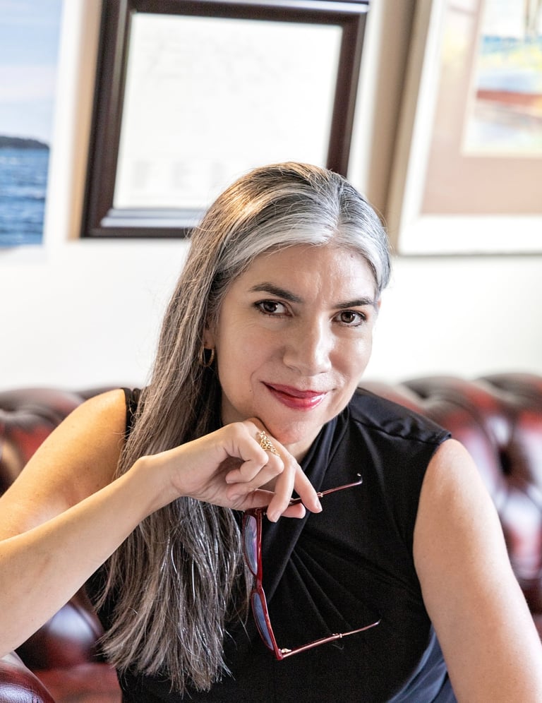 Poet Sheena Powell seated and smiling, with long silver-streaked hair, wearing a black sleeveless top