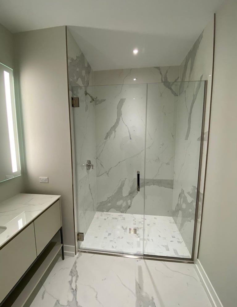 Modern master bathroom featuring a walk-in glass shower with marble walls and mosaic tile flooring.