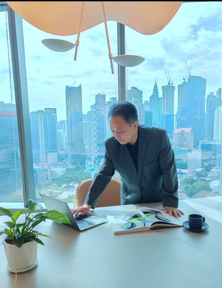 Professional businessman in a suit working on a laptop in a high-rise office with a city skyline view.
