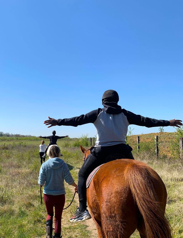 un jeune homme monté à cheval écartant grand les bras lors d'une séance d'équithérapie