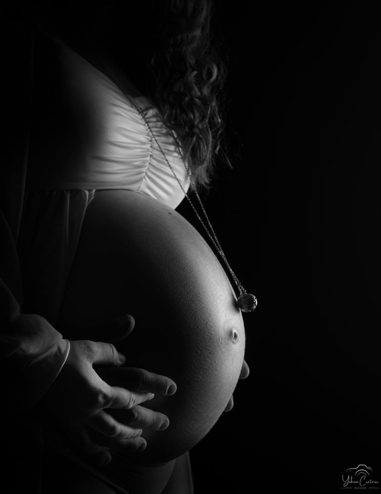 Black and white maternity photography profile of a pregnant woman's belly with hands and necklace.