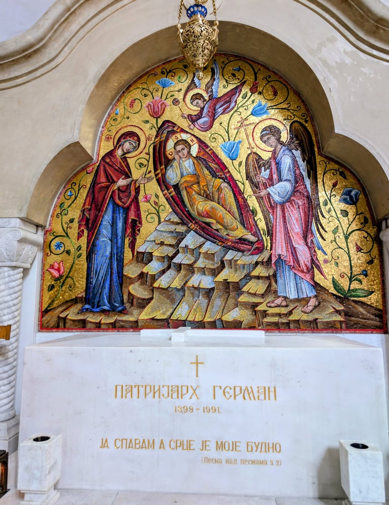 A colorful Byzantine mosaic of a religious scene above a white marble tomb in an Orthodox church.