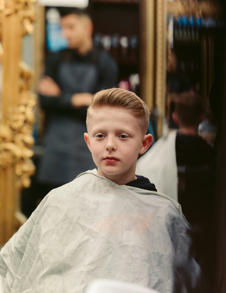Niño pequeño con corte pompadour estilizado usando capa en una barbería profesional.