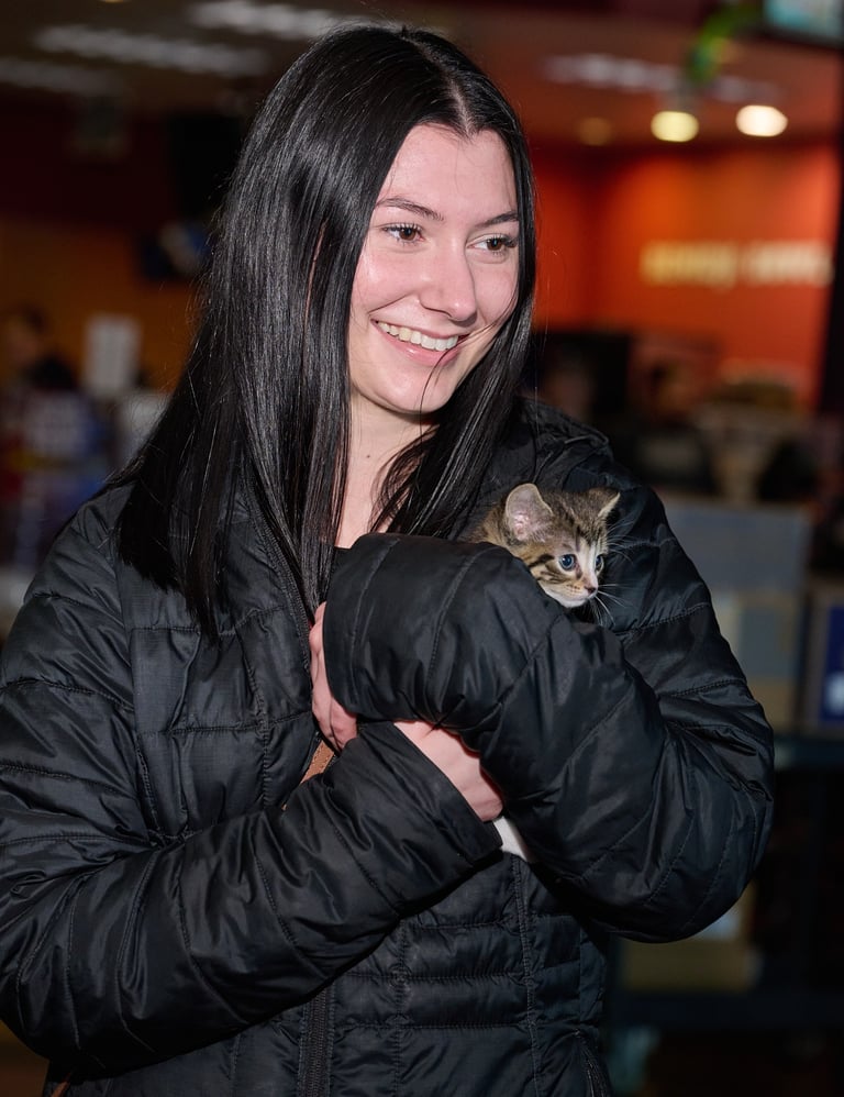 a woman in a black jacket holding a kitten looking at the same direction