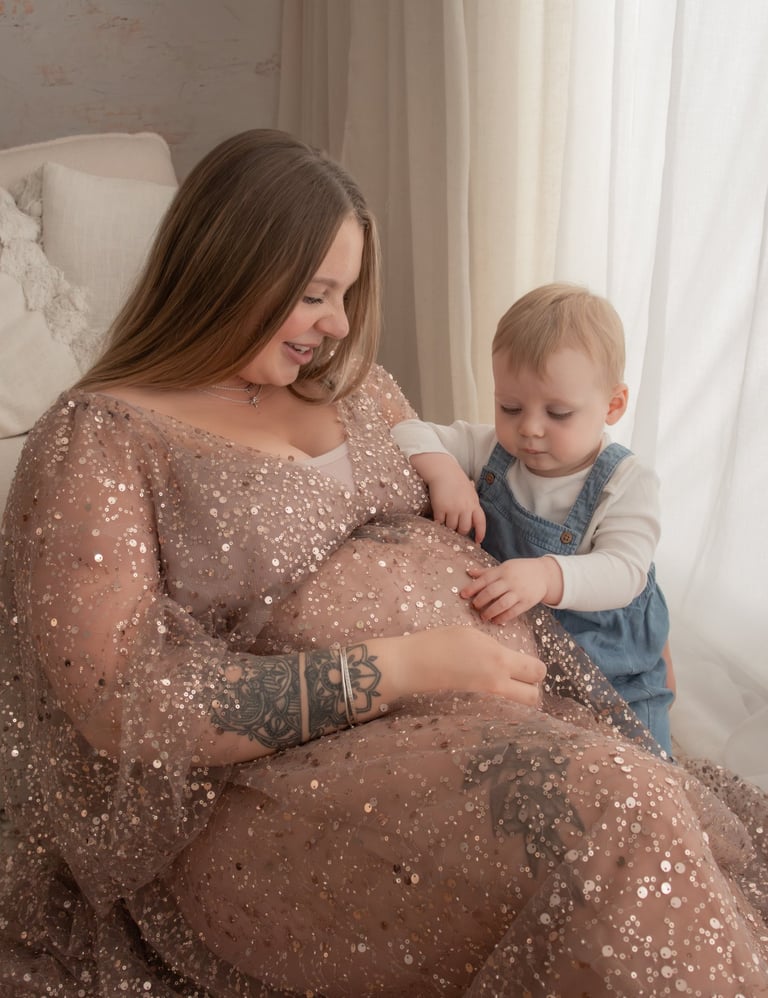 A pregnant mother in a sequin maternity gown sitting with her toddler during a maternity photoshoot.