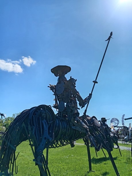 Rustic metal sculpture of Don Quichotte on a horse holding a spear in an outdoor art garden.