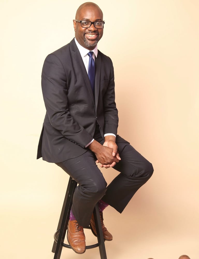 a man in a suit and tie sitting on a stool