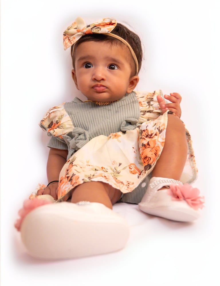 a baby girl sitting on a white surface