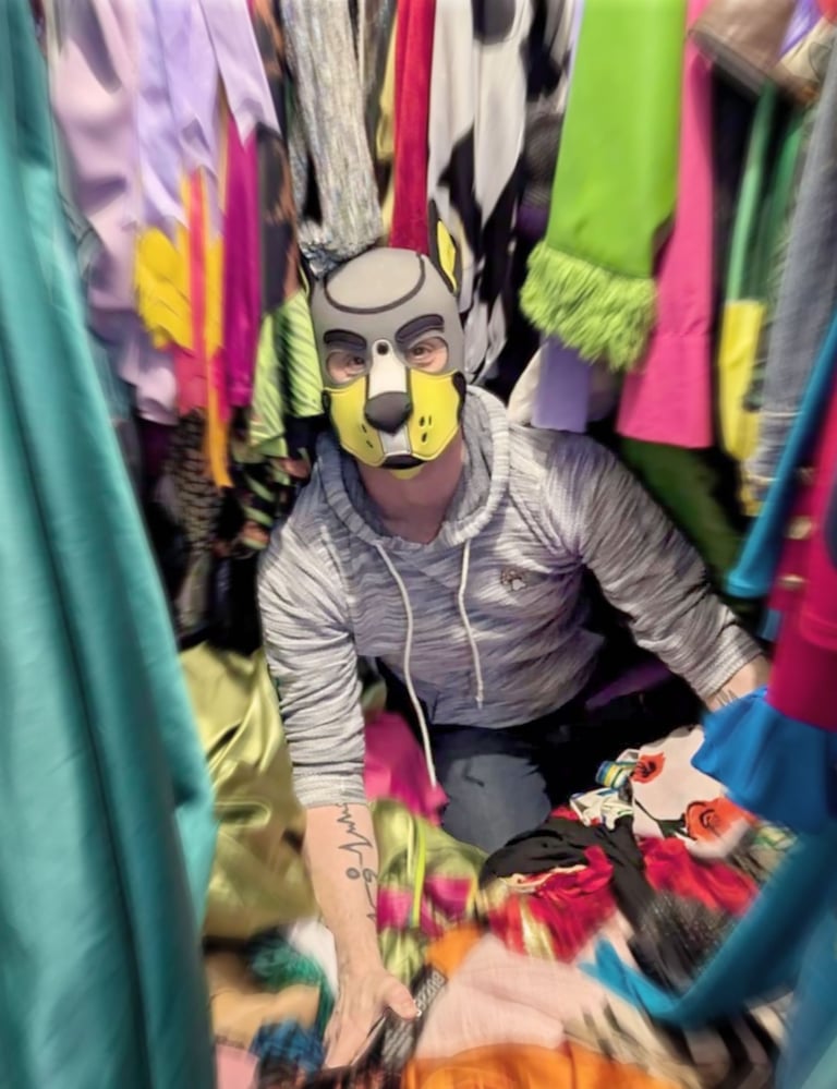 Man in pup mask sitting in his closet.