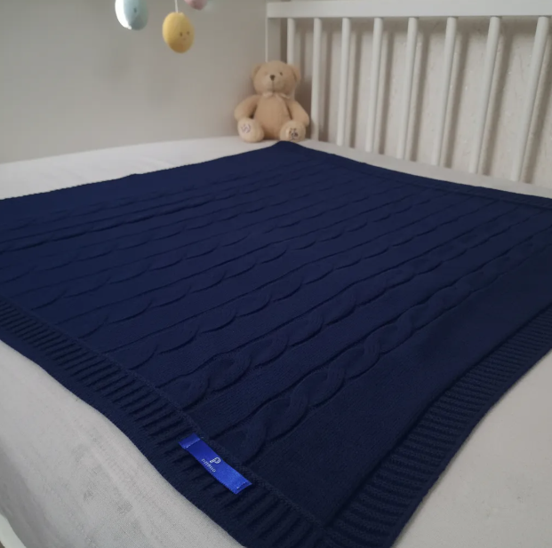 Manta Cobertor com desenho de trança em cima de um berço como ambientação