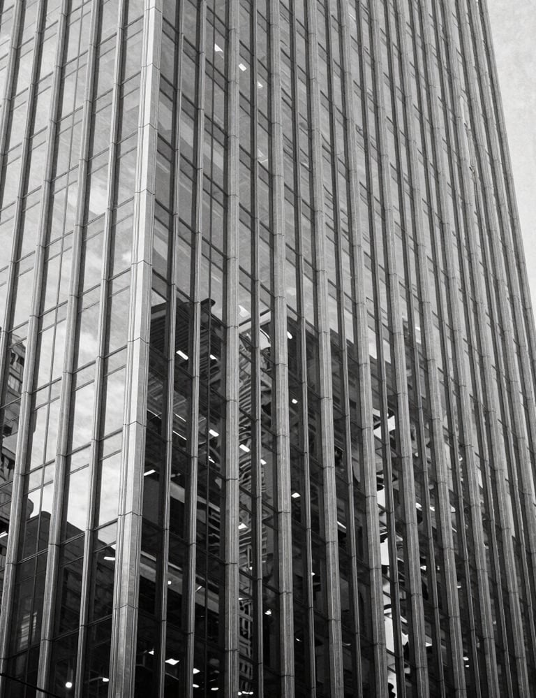 A professional black and white architectural photograph of a sleek skyscraper in a North American / US city. The shot focuses on the geometric patterns of the glass facade, exuding contemporary elegance and clean, minimalist lines.