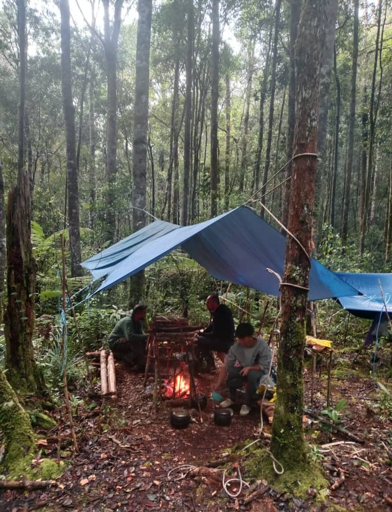 a group of people sitting around a fire pit underneath the tarpaulin during the jungle survival trip