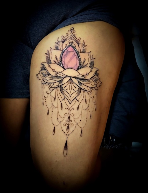 Tatuaje ornamental de flor de loto en el muslo, con una gema rosa y detalles de joya.