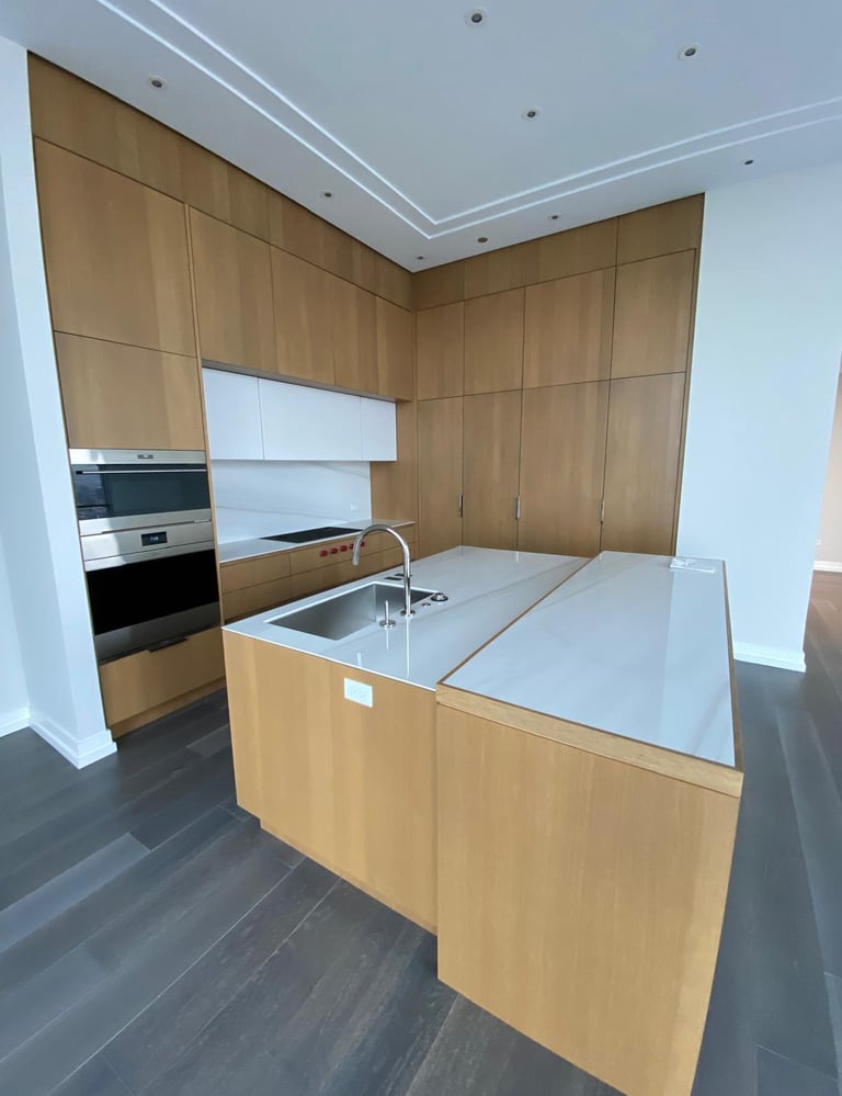 Modern luxury kitchen featuring light oak wood cabinetry, white quartz countertops, and a large island with a sink.