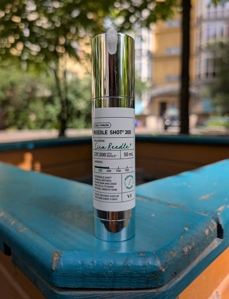 A bottle of VT Cosmetics Reedle Shot 300 facial essence sits on a blue wooden ledge outdoors.