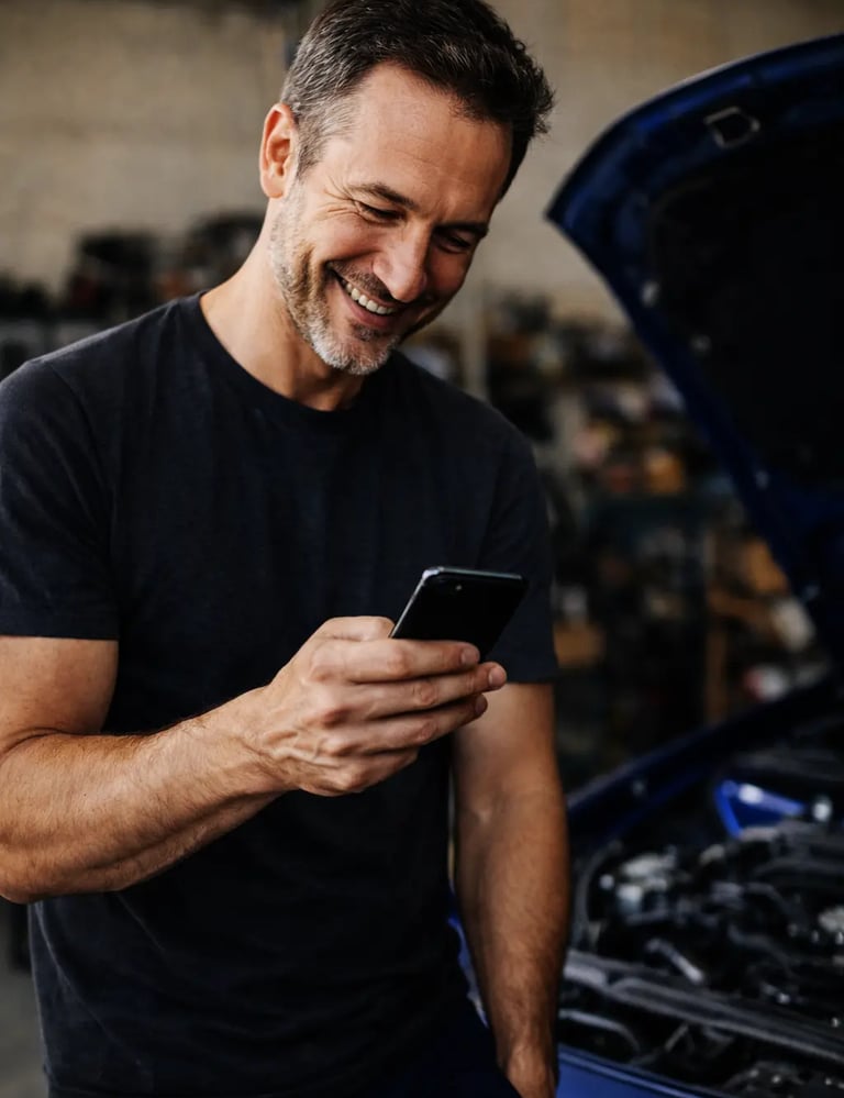 Meccanico sorride guardando lo smartphone, supporto Hulemex online che accompagna e spiega i prodott