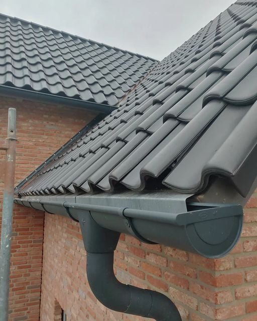 Toiture en tuiles noires avec gouttière en PVC anthracite – finition soignée sur façade en briques.