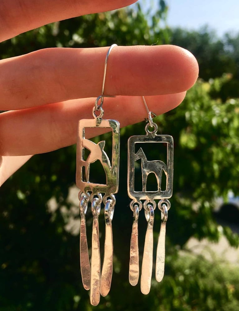 a pair of earrings with a horse and a swallow on it