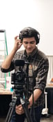 a man in a plaid shirt and headphones on a tripod recording video