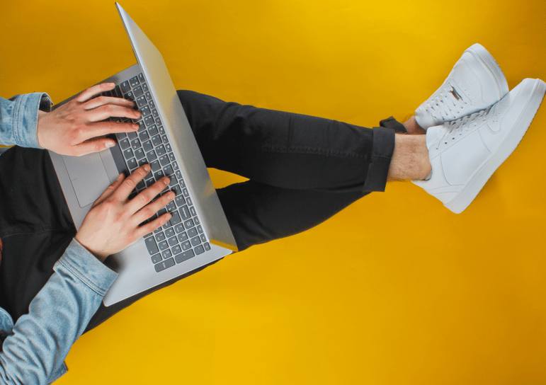a man sitting on a yellow floor with a laptop propped on his legs