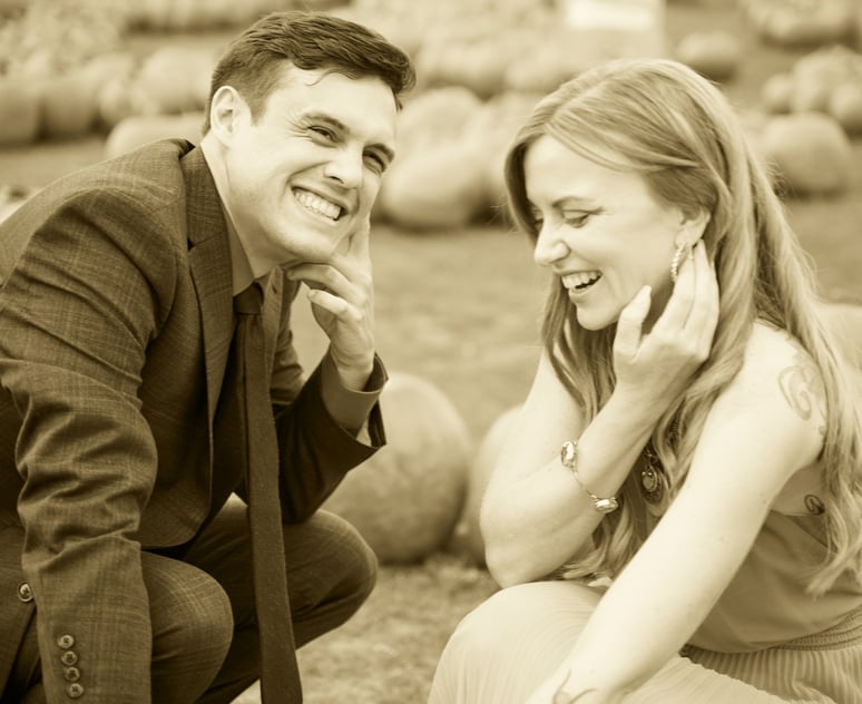 a man and woman in a field of pumpkins smiling in sepia style