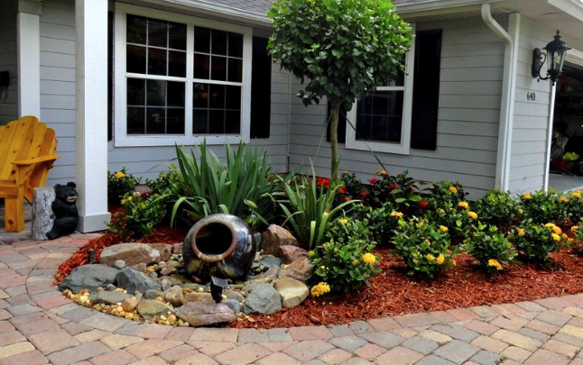 a garden with a fountain and a bench in front of a house