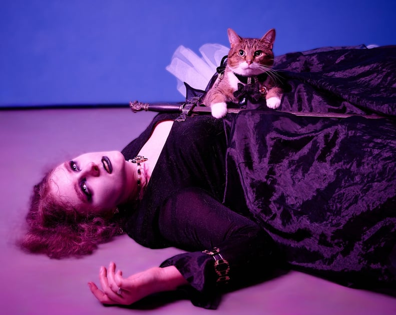 a girl in a black dress dying on the ground with a cat holding a sword on top of her body