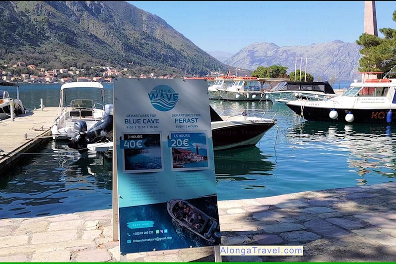 A sign by the bay with boats saying: 'Blue cave tour'