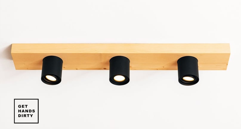 Image of a concrete ceiling with a wood block attached. The wood block has black spotlights fixtures