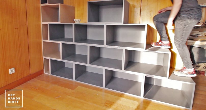 A person going up a staircase that is simultaneously a shelf.