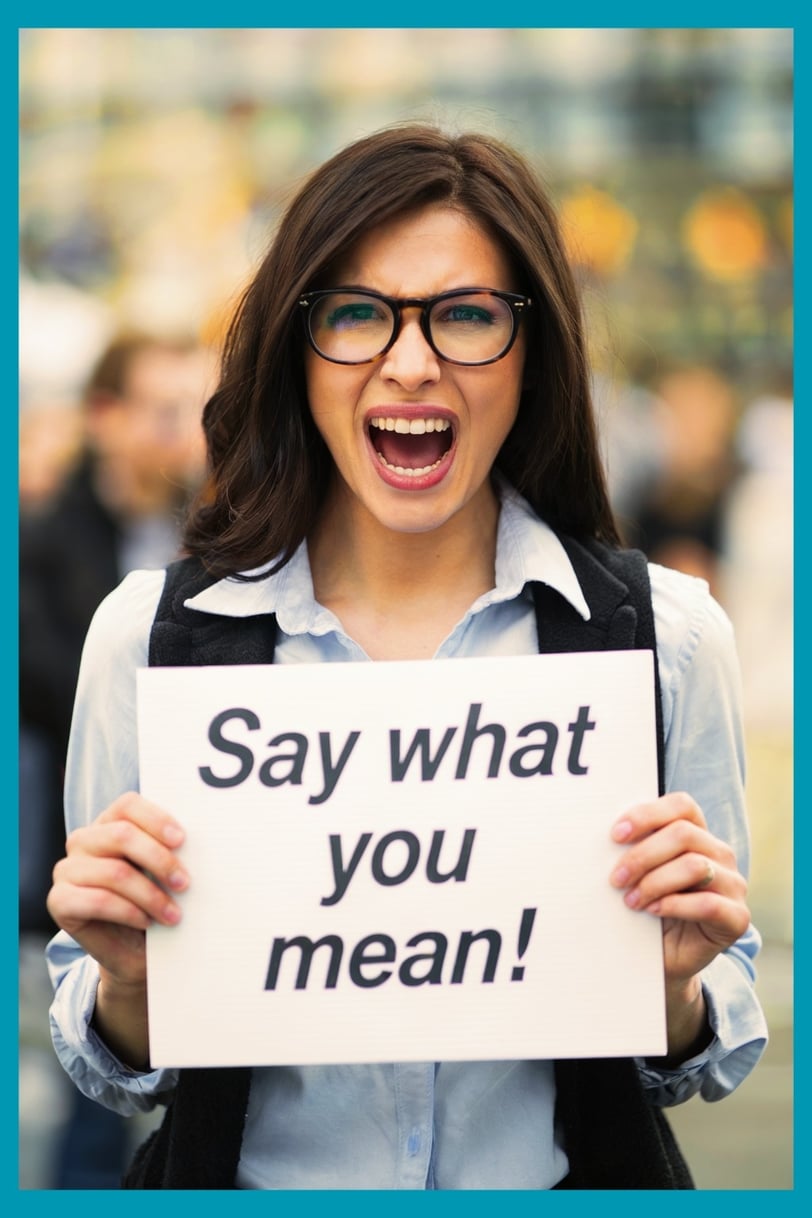 a woman holding a sign saying say what you mean