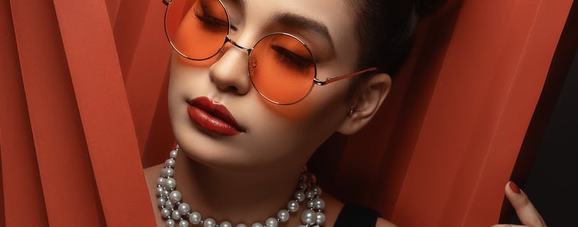 Foto de mulher utilizando óculos com lentes laranja e colar de pérolas.